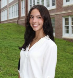 A woman is smiling for the camera while standing outdoors on grass.
