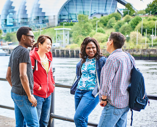 Newcastle Students A group of people is standing on a bridge, enjoying the outdoors. They are smiling